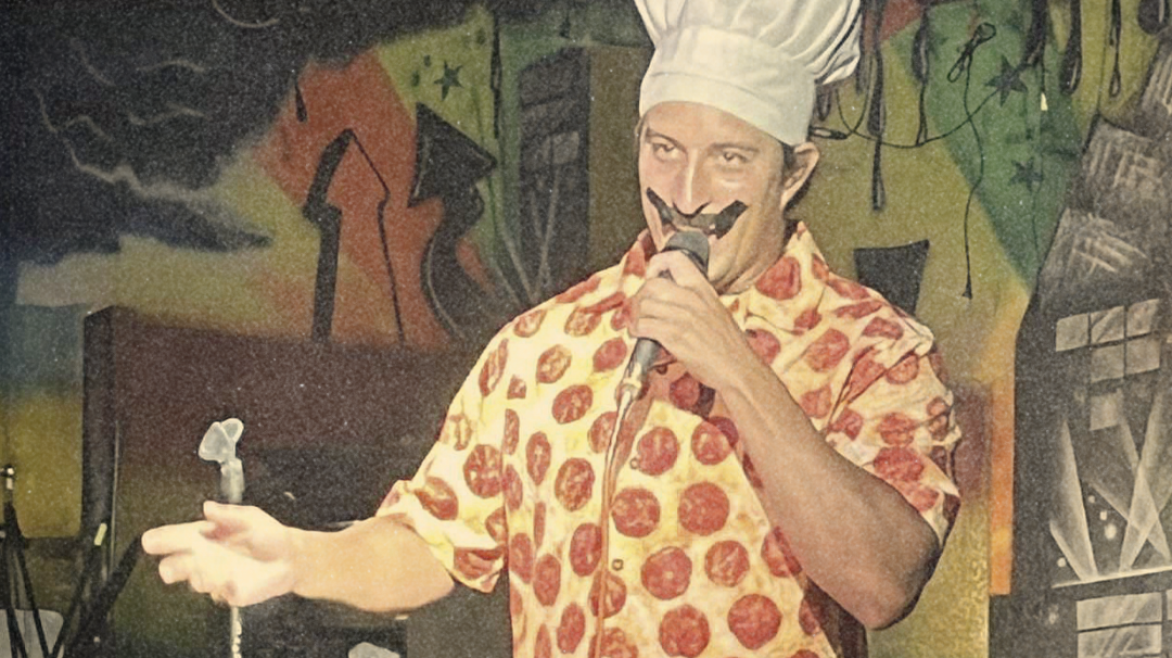 Tony Pepperoni performing on Kill Tony in a pepperoni-print shirt and oversized chef’s hat at Anderson Mill in Austin.